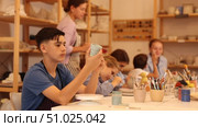 Interested children of different ages painting ceramic objects with teacher in art studio. Стоковое видео, видеограф Яков Филимонов / Фотобанк Лори