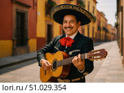 Smiling mariachi musician in traditional charro suit and sombrero playing guitar on a vibrant street with colorful colonial buildings. Стоковое AI-изображение, AI-художник Башкирова Анна / Фотобанк Лори