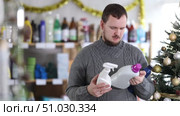 In Christmas decorated shop, man examines product and doubts, chooses laundry fabric softener and and tile cleaner spray, study items properties in household department. Стоковое видео, видеограф Яков Филимонов / Фотобанк Лори