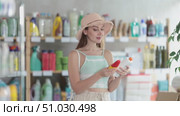 European woman stands in a supermarket and chooses a protective sunscreen, SPF, comparing manufacturers and the degree of protection from sunlight. Woman in summer clothes and hat buying tanning products. Стоковое видео, видеограф Яков Филимонов / Фотобанк Лори