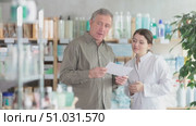 In sales area of drugstore, mature man with prescription intently looks at display cases, trying to find vitamin for adults in open display. Girl pharmacist offer help to customer. Стоковое видео, видеограф Яков Филимонов / Фотобанк Лори