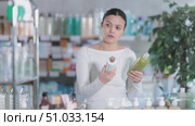 Asian woman stands in a pharmacy and holds shampoos in her hands and chooses between them. Adult woman buying shampoo at pharmacy. Стоковое видео, видеограф Яков Филимонов / Фотобанк Лори