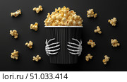 Spooky popcorn in a skeleton-themed cup for Halloween celebrations. Стоковое AI-изображение, AI-художник Katsiaryna Repich / Фотобанк Лори