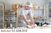 Young male baker prepares raw yeast dough in bakery, shaping it into a baguette and rolls dough to give the shape of future bread. Стоковое видео, видеограф Яков Филимонов / Фотобанк Лори