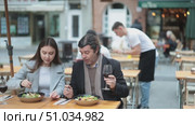 Joyful husband and wife sit on the terrace of a restaurant in warm outerwear and chat, they drink red wine and discuss food. Стоковое видео, видеограф Яков Филимонов / Фотобанк Лори