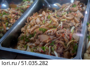 Traditional Asian dish of pork offal with spicy sauce and fresh vegetables. Finely chopped pieces of meat are mixed with herbs, chili peppers, onions and spices, creating a rich aroma and spicy taste. Served in gastronorm containers at the market or in a street cafe. Стоковое фото, фотограф Анна Кривицкая / Фотобанк Лори