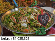 A large metal platter with a mouth-watering dish of crabs fried with vegetables and herbs in a fragrant sauce. The bright orange shells of the crabs contrast with the rich green of the vegetables, creating a colorful and tasty composition. In the foreground is a heart-shaped price tag, emphasizing the atmosphere of a street market. Стоковое фото, фотограф Анна Кривицкая / Фотобанк Лори