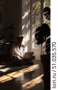 Man working calmly on a laptop in a sunlit room with plants during a serene afternoon. Стоковое AI-изображение, AI-художник Сергей Толмачёв / Фотобанк Лори