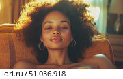 A woman with beautiful curly hair enjoys a peaceful moment on a couch, illuminated by warm afternoon sunlight coming through the window. Стоковое AI-видео, аниматор Данила Большаков / Фотобанк Лори