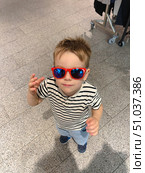 A playful young boy wearing red sunglasses and a striped shirt poses confidently indoors. Стоковое фото, фотограф Виктор Ветошкин / Фотобанк Лори