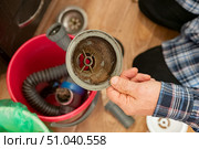 A hand holds a dirty vacuum filter above a red bucket filled with debris and vacuum parts, highlighting the cleanup process in a contemporary kitchen environment. Стоковое фото, фотограф Вербицкая Светлана / Фотобанк Лори