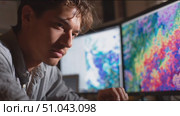 Young man analyzes colorful data visualizations while working on dual monitors in a modern workspace. Стоковое AI-видео, аниматор Сергей Толмачёв / Фотобанк Лори