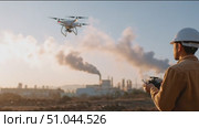 Operator controls drone at industrial site as smoke rises from factories during sunset. Стоковое AI-видео, аниматор Сергей Толмачёв / Фотобанк Лори