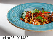 Korean udon noodle dish with shrimp, squid, red pepper and fresh herbs served in a rustic blue plate on white background. Стоковое фото, фотограф Aleksandr Gavrilychev / Фотобанк Лори