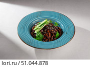 Traditional Korean jajangmyeon noodles with rich black bean sauce, fresh cucumber, sesame seeds and herbs served in a rustic blue ceramic bowl. Стоковое фото, фотограф Aleksandr Gavrilychev / Фотобанк Лори