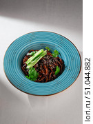Traditional Korean jajangmyeon noodles with rich black bean sauce, fresh cucumber, sesame seeds and herbs served in a rustic blue ceramic bowl. Стоковое фото, фотограф Aleksandr Gavrilychev / Фотобанк Лори
