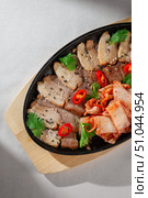 Sliced pork belly served on cast iron plate with traditional Korean kimchi, fresh cilantro, black sesame seeds and red chili peppers for garnish. Стоковое фото, фотограф Aleksandr Gavrilychev / Фотобанк Лори