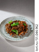 Traditional Korean dish made of stir-fried seaweed and pork with onions, red chili sauce and fresh herbs served on a rustic ceramic plate. Стоковое фото, фотограф Aleksandr Gavrilychev / Фотобанк Лори