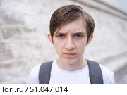 Портрет 12-летнего рассерженного мальчика в белой футболке, с рюкзаком на улице летом. Стоковое фото, фотограф Яна Проничева / Фотобанк Лори