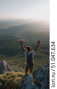 Person stands on rocky ledge with arms outstretched over a vast valley during sunset in a mountainous region. Стоковое AI-видео, аниматор Сергей Толмачёв / Фотобанк Лори