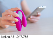 A woman synchronizes a modern curved clitoral vaginal vibrator with a smartphone. The girl has online sex using a toy. Стоковое фото, фотограф Михаил Решетников / Фотобанк Лори