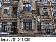 The facade of a historic building in St. Petersburg with rich decorative decoration. The central part is decorated with stucco in the form of lion heads framing an arched window with carved elements and plant ornaments. The window sill is decorated with floral motifs, and around the windows there are columns with carved leaves and architectural details. The color of the facade is beige-terracotta with white elements of stucco, in places traces of time and abrasions are visible, giving the building a special charm of the old architecture of St. Petersburg. The balconies have forged gratings, creating an atmosphere of the early 20th century. Стоковое фото, фотограф Анна Кривицкая / Фотобанк Лори