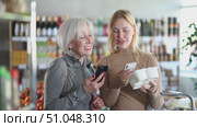 Girl with senior female relative in store scan QR code on yogurt label. In mobile app, buyer receive information about yogurt. They check manufacturer data in registry database of national agency. Стоковое видео, видеограф Яков Филимонов / Фотобанк Лори