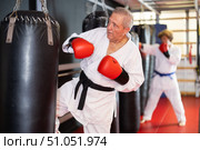 Senior man in white gi training with punching bag in dojo. Стоковое фото, фотограф Яков Филимонов / Фотобанк Лори