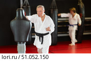 Elderly man in white kimono trains in gym - he punches sports dummy. Стоковое фото, фотограф Яков Филимонов / Фотобанк Лори