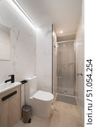 Modern bathroom with marble walls, a shower, toilet, and sink. Bright lighting enhances the clean, minimalist design. Стоковое фото, фотограф PAv / Фотобанк Лори
