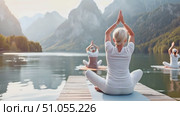 A group of individuals are practicing yoga on a dock by the water, performing various poses and stretches under the open sky. Стоковое AI-видео, аниматор Данила Большаков / Фотобанк Лори