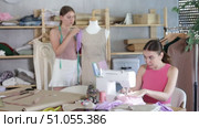 Two qualified dressmakers work in a sewing workshop against the backdrop of racks with fabrics and sewing accessories. Young women at a sewing workshop. Стоковое видео, видеограф Яков Филимонов / Фотобанк Лори