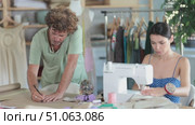 Attentive middle-aged male dressmaker drawing on paper using curves while woman sewing in workshop. Стоковое видео, видеограф Яков Филимонов / Фотобанк Лори
