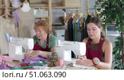 Two seamstresses work together and sew a collection of clothes on sewing machines in the workshop. Female dressmakers sitting at a table and sewing clothes to order. Стоковое видео, видеограф Яков Филимонов / Фотобанк Лори