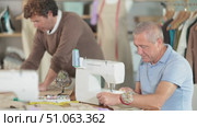Elderly man tailor sews on machine adult man assistant drawing pattern on paper in workshop. Стоковое видео, видеограф Яков Филимонов / Фотобанк Лори