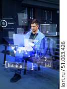 Young man using laptop in urban setting with digital interface projections during daytime. Стоковое фото, фотограф Сергей Толмачёв / Фотобанк Лори