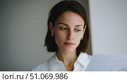 A woman with short dark hair and a white blouse is looking thoughtfully at a document or paper in front of her. Her expression is calm and focused, possibly suggesting she is reading something important or personal. The natural lighting and neutral background give the image a serene and introspective feel. Стоковое AI-изображение, AI-художник Ксения Чунаева / Фотобанк Лори