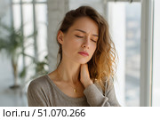 Красивая молодая девушка, держащаяся руками за шею от боли, стоит в ярком современном интерьере. Стоковое AI-изображение, AI-художник Максим Коломыченко / Фотобанк Лори