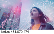 A young woman stands in a city, looking up at the cityscape with a network overlay. She is looking hopeful and optimistic. Стоковое AI-видео, аниматор Данила Большаков / Фотобанк Лори