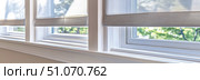 Bright interior window with white frame and modern fabric roller shades, allowing soft natural light and green outdoor blur to filter into the room. Стоковое AI-изображение, AI-художник Катерина Бондарец / Фотобанк Лори