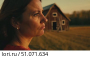 A woman reflects deeply while standing in a golden field near a rustic barn during sunset. Стоковое AI-видео, аниматор Данила Большаков / Фотобанк Лори