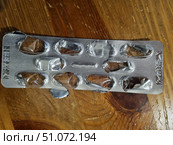 A blister pack of medicinal capsules or tablets, located on a wooden surface. Most of the cells are empty, the protective foil is partially opened, indicating that the doses of the drug have already been used. The packaging is made of transparent plastic with aluminum foil on the back. Embossed markings indicating the batch and expiration date of the drug are visible on the foil. The picture conveys a realistic scene of everyday use of medications associated with the treatment or prevention of diseases. Стоковое фото, фотограф Анна Кривицкая / Фотобанк Лори