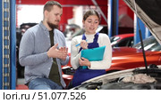 Uniformed car service workers discuss the process of repairing a car. Mechanic with tools tells what parts he replaced and repaired, and the manager writes down. Стоковое видео, видеограф Яков Филимонов / Фотобанк Лори