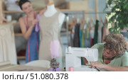 Focused middle-aged tailor using sewing-machine and tailoress working with dummy in workshop. Стоковое видео, видеограф Яков Филимонов / Фотобанк Лори