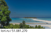 A sandbar winds through the aquamarine ocean to a small tropical island. Silhouettes of boats, people on the beach. A frame of green trees in the foreground. Clear blue sky. Copy space. Madagascar. Стоковое фото, фотограф Вера Ивановна Кубарева / Фотобанк Лори