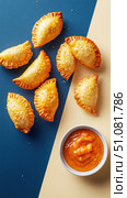 Crispy empanadas gracefully float against a bold split-color backdrop. Their golden crust contrasts with the deep navy and creamy off-white, creating a striking visual impact. Стоковое AI-изображение, AI-художник Nart / Фотобанк Лори