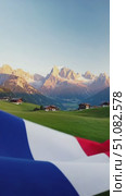 A close-up of the French flag waving in the foreground with a scenic mountain landscape in the background. The sky is clear and blue, enhancing the vibrant colors of the flag. Стоковое AI-видео, аниматор Nart / Фотобанк Лори