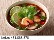 Bowl of Tom Yum Shrimp and Mushroom hot soup, garnished with fresh coriander leaves, herbs, lime slices, chili peppers. Beige table background, chopsticks pair. Traditional Thai Prawn Tom Yum Soup. Стоковое AI-изображение, AI-художник Марина Демидюк / Фотобанк Лори