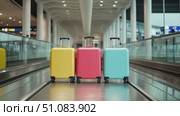 Three colorful suitcases in an airport terminal. The suitcases are yellow, pink, and blue, placed on a moving walkway. The background shows a modern airport design. Стоковое AI-видео, аниматор Nart / Фотобанк Лори