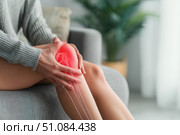 Knee pain icon. Joint pain, Arthritis and tendon problems. Woman in jeans sitting sofa, touching nee at pain point. Mature person feeling unwell, suffering from pain in leg. Red effect painful injury. Стоковое AI-изображение, AI-художник Марина Демидюк / Фотобанк Лори